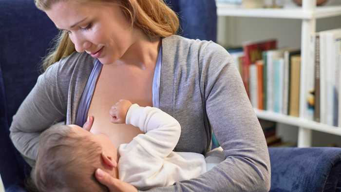 A mother breastfeeds a baby in the cross cradle hold position.