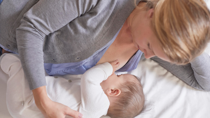 A mother breastfeeds a baby in the side lying hold position.